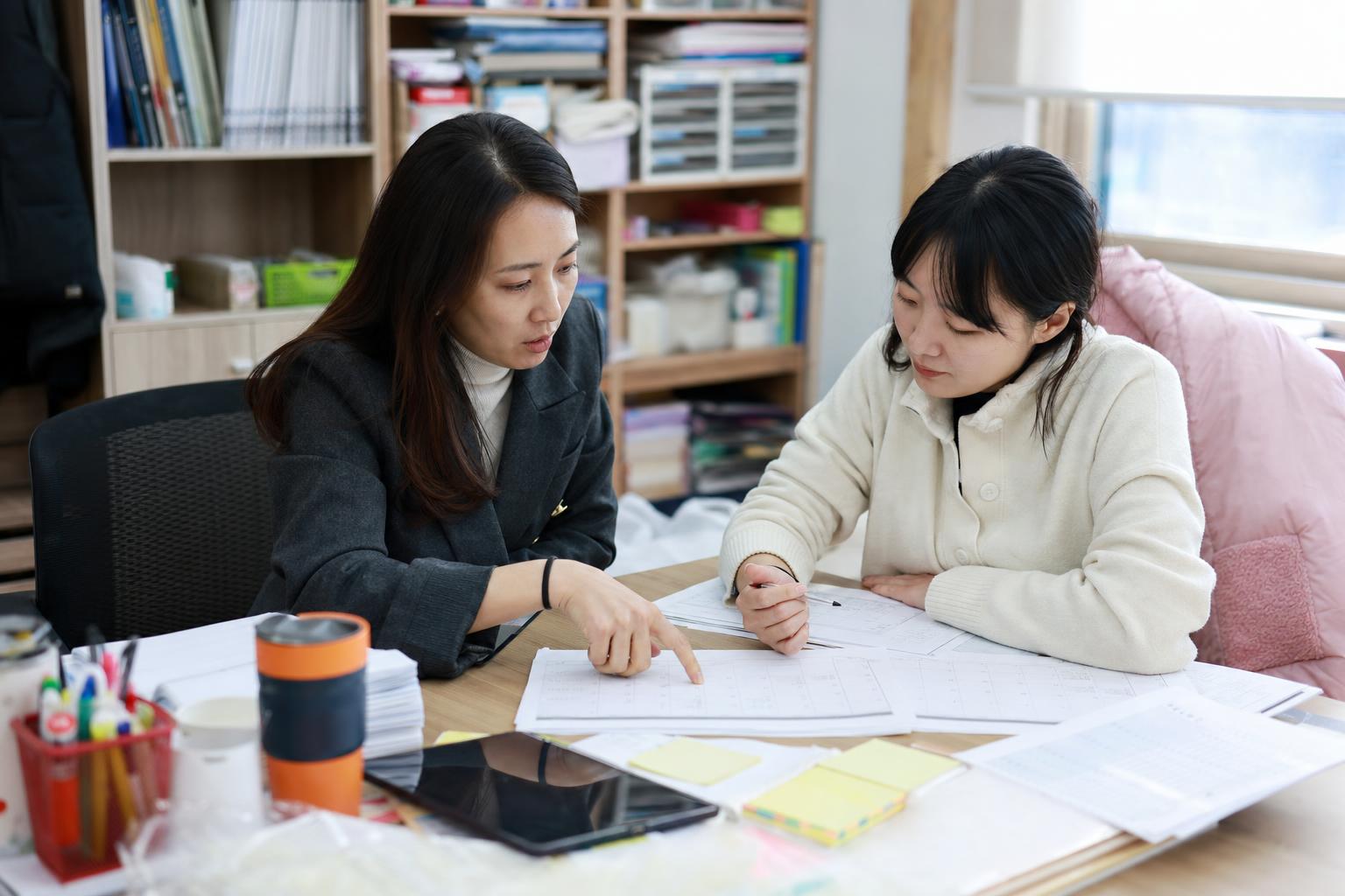 학원 교무실에서 보강 후보 시간을 두 가지로 좁혀 확인하는 실사진형 장면